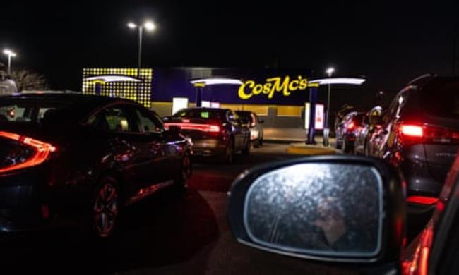 A car rear window in front of other cars and neon sign reading ‘CosMc’s’